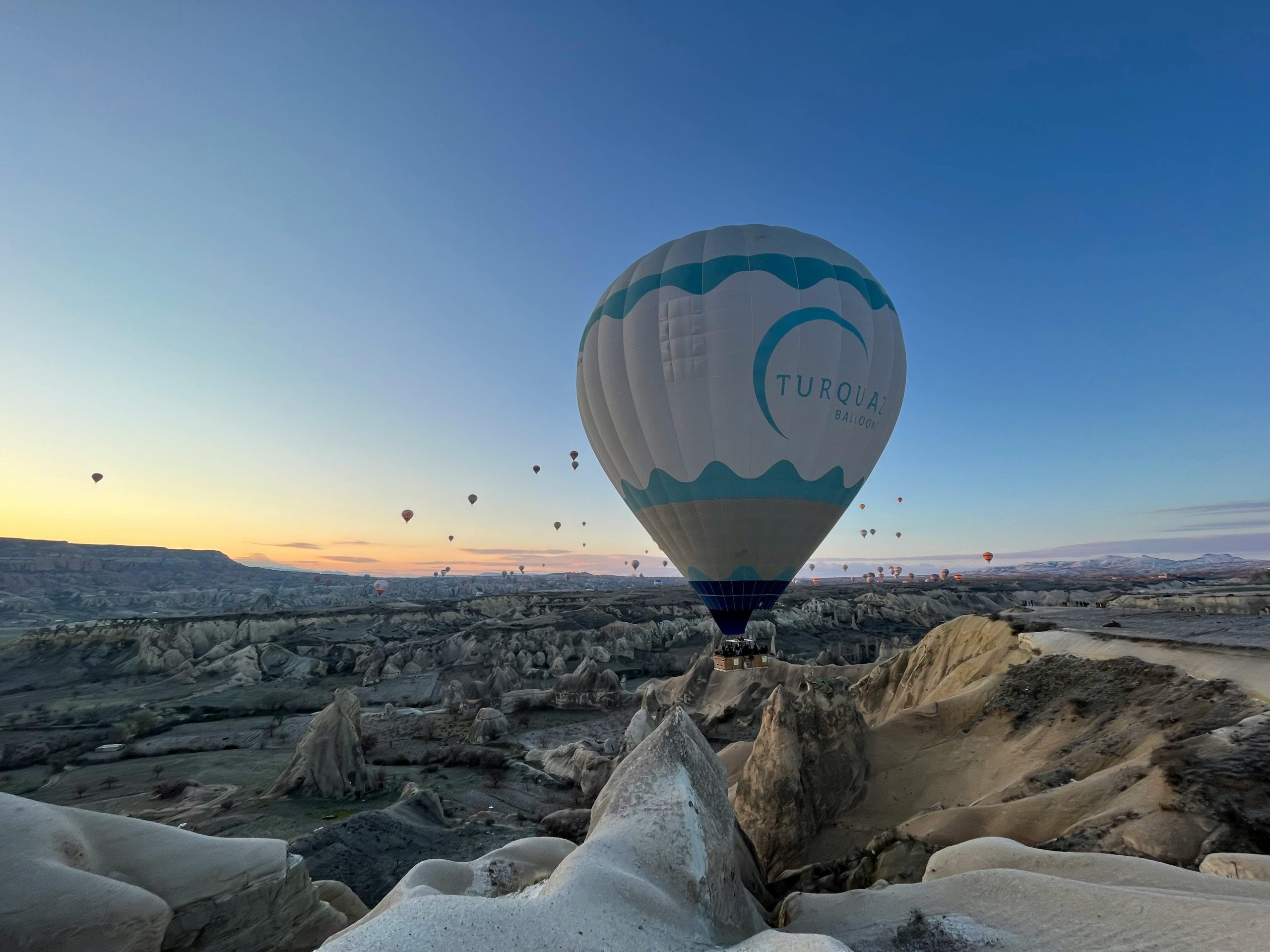 Breathtaking view of hot air balloons floating over Cappadocia's rock formations at sunrise.