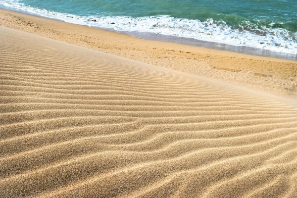 Golden sand ripples leading to turquoise waves at La Guajira beach, Colombia.