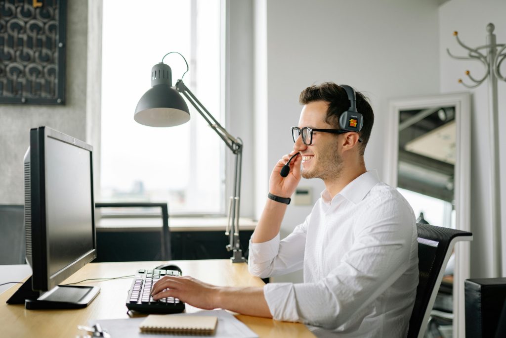 Smiling man wearing headset working at computer in bright office.